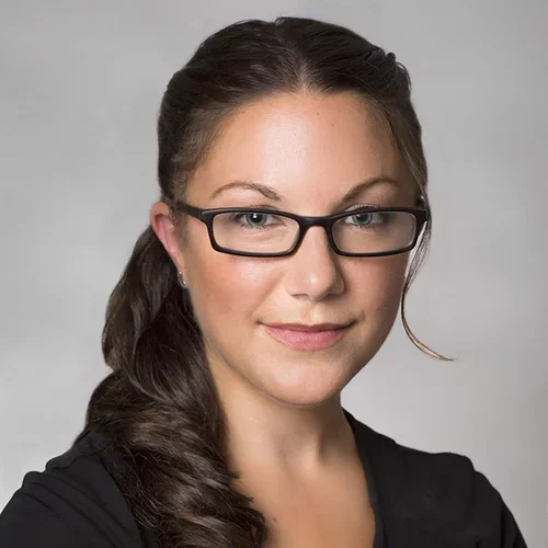 a woman with long dark brown hair and glasses against a gray background