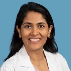 A woman with long black hair, wearing a pink shirt under her white doctors coat