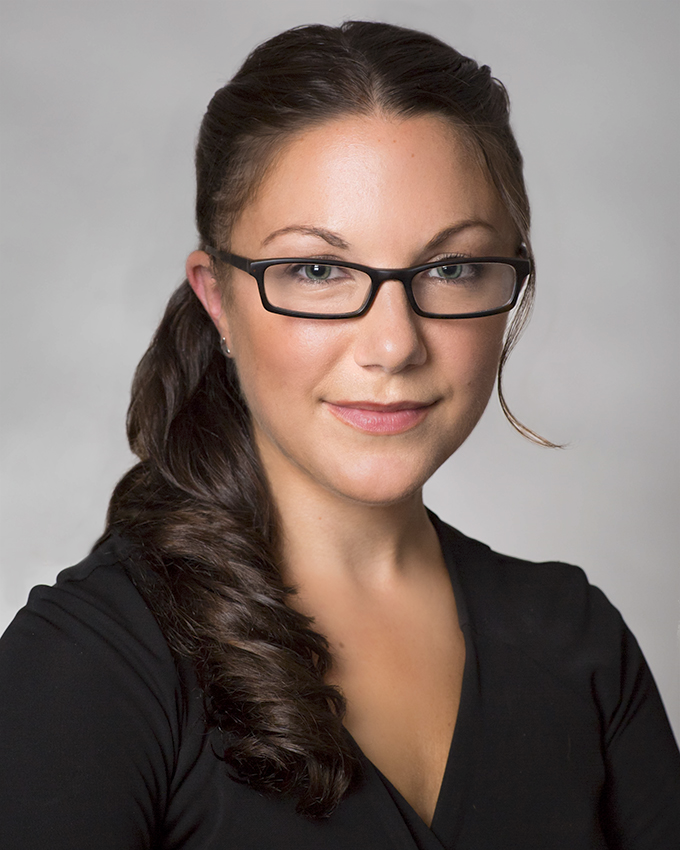 image of a woman with long dark brown hair and glasses against a gray background
