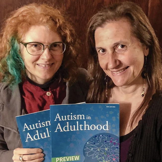 Two women holding a book titled 'Autism in Adulthood'